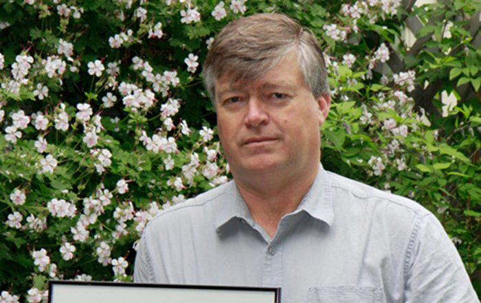 A man (Kees Govers) holding an award with flowers in the background.