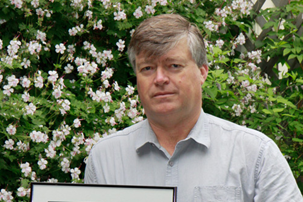 A man (Kees Govers) holding an award with flowers in the background.
